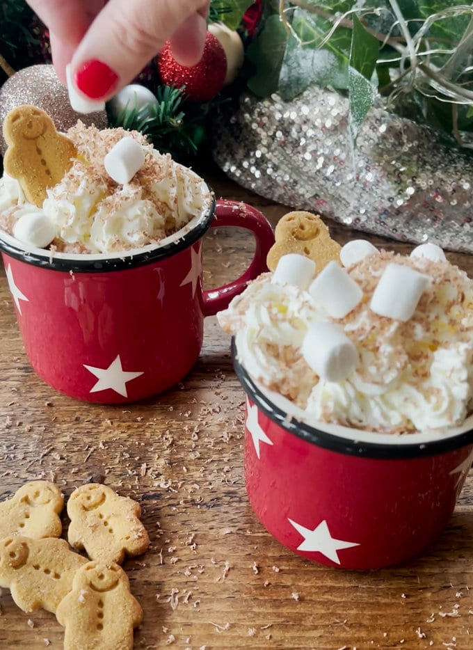 Decoration being added to the hot chocolate. Whipped cream, grated chocolate along with mini marshmallows and gingerbread men.