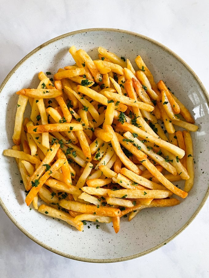 Airfried crispy fries served in a round bowl and garnished with salt and chopped parsley.