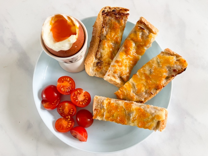 Airfryer Sausage & Cheese Soldiers served on a blue plate with a dippy egg and sliced cherry tomatoes