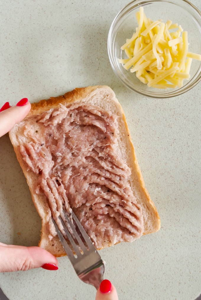 Sausage meat being spread onto a slice of white bread with a fork.