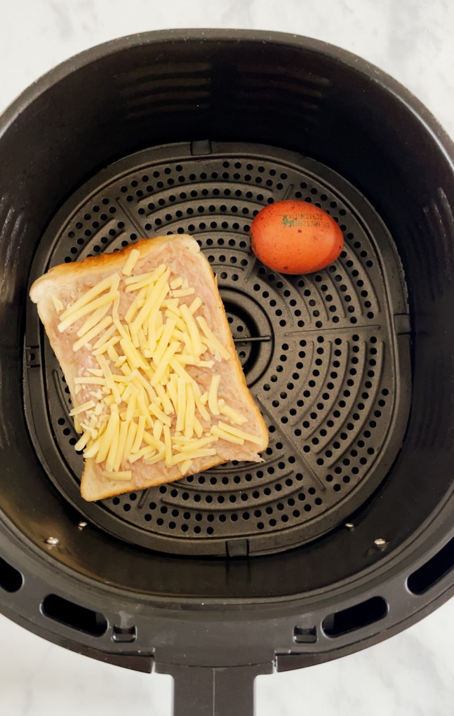 Slice of bread with sausage meat and cheese on top added to the airfryer along with one egg.