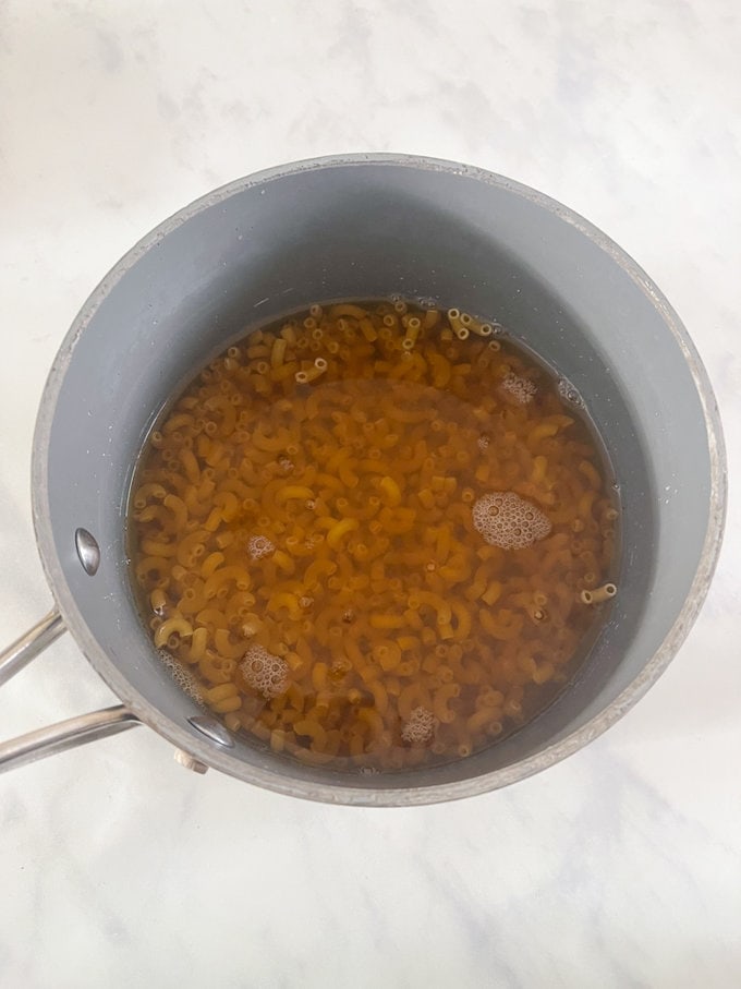 Noodles placed in a pan of bone broth, ready to cook.