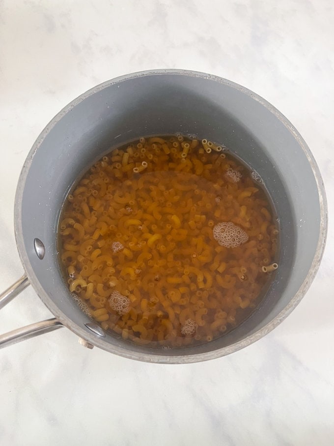 Pasta added to a pan of bone broth, ready for cooking.