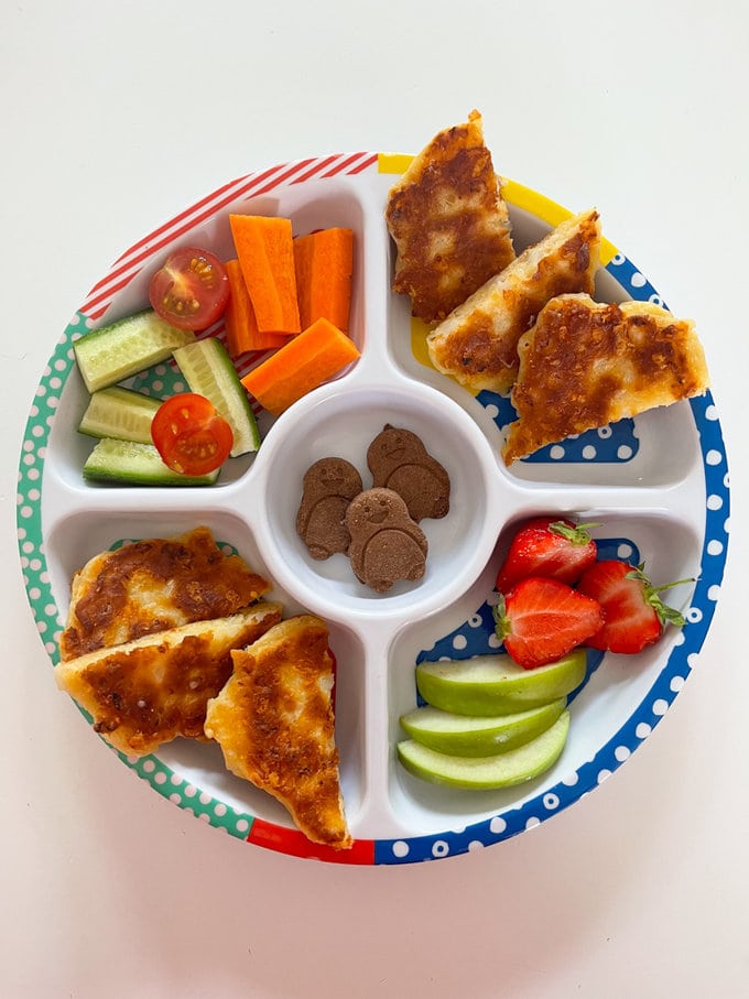 Cauliflower cheese fritters presented on a child's pick plate. along side fresh fruit and vegetables.