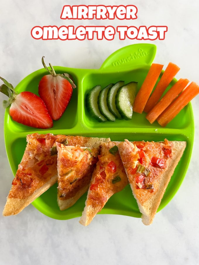 Air Fryer Omelette Toast served on a green children's plate with chopped strawberries, cucumber and carrot