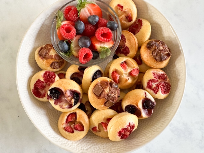 Easy breakfast recipes and prep ideas for kids - Mini pancake bites served in a white bowl with a casserole dish with chopped fresh berries