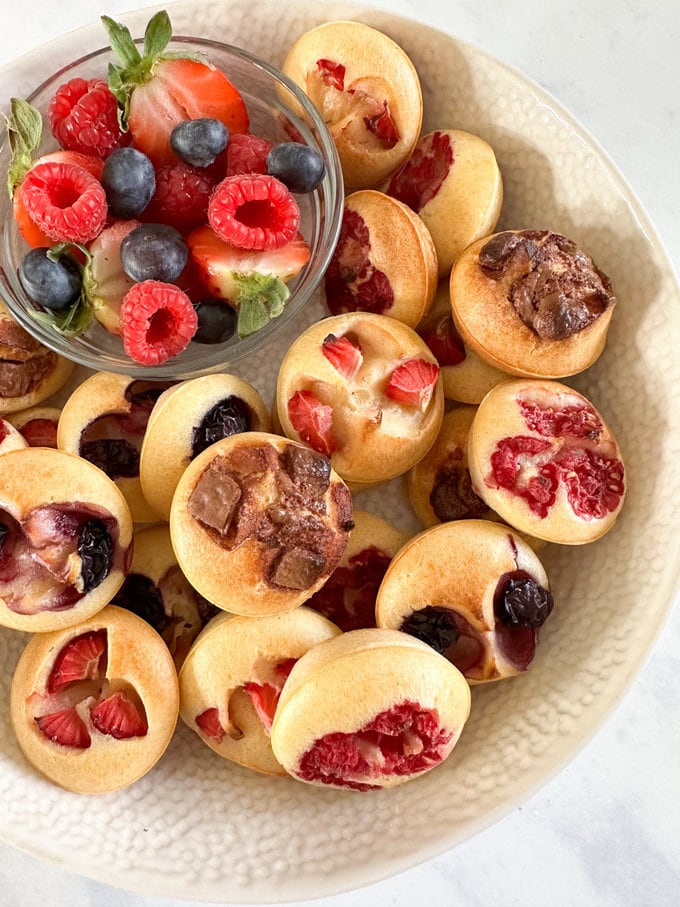 Mini pancake bites served in a large bowl, and a small bowl of fresh berries on the side.