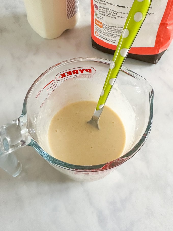 Pancake batter being mixed with a green spotty spoon in a Pyrex glass jug.