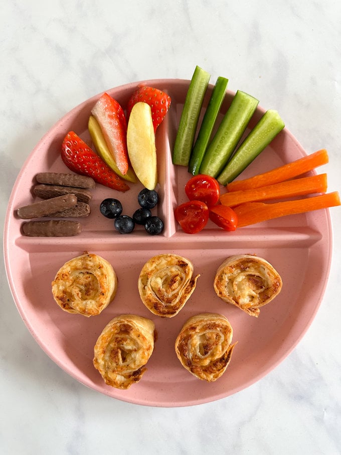 Chicken & Cheese pinwheels served on a pink plate served with fresh berries,cucumber,carrots and cherry tomatoes.