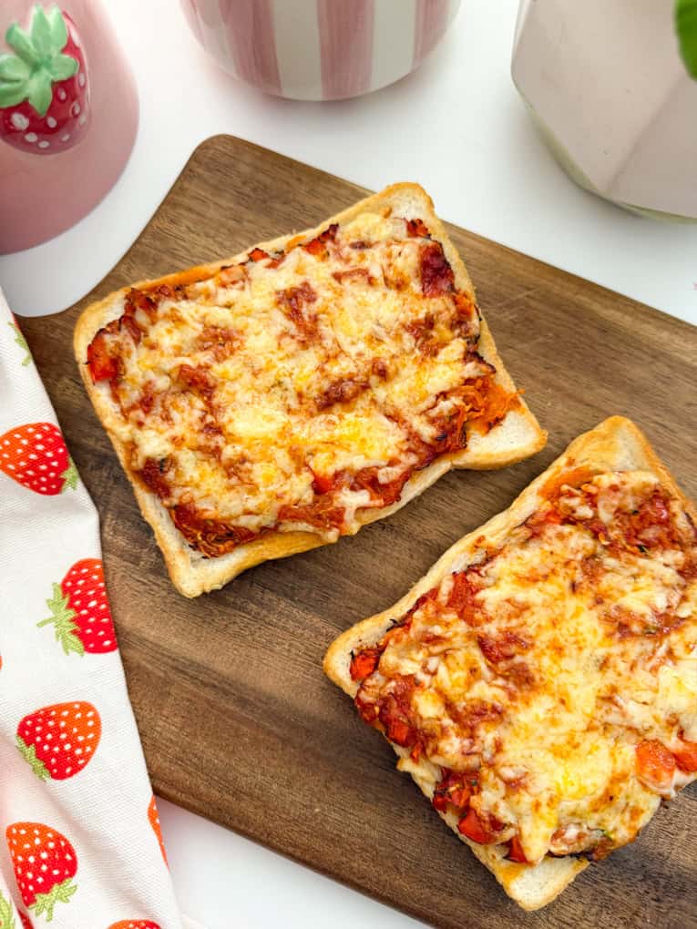 Two full slices of Air fryer pizza toast on a wooden chopping board.