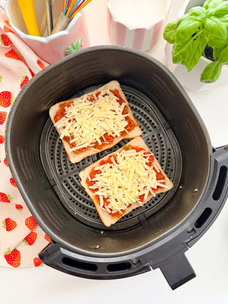 Two slices of pizza toast in the air fryer drawer ready to be cooked.