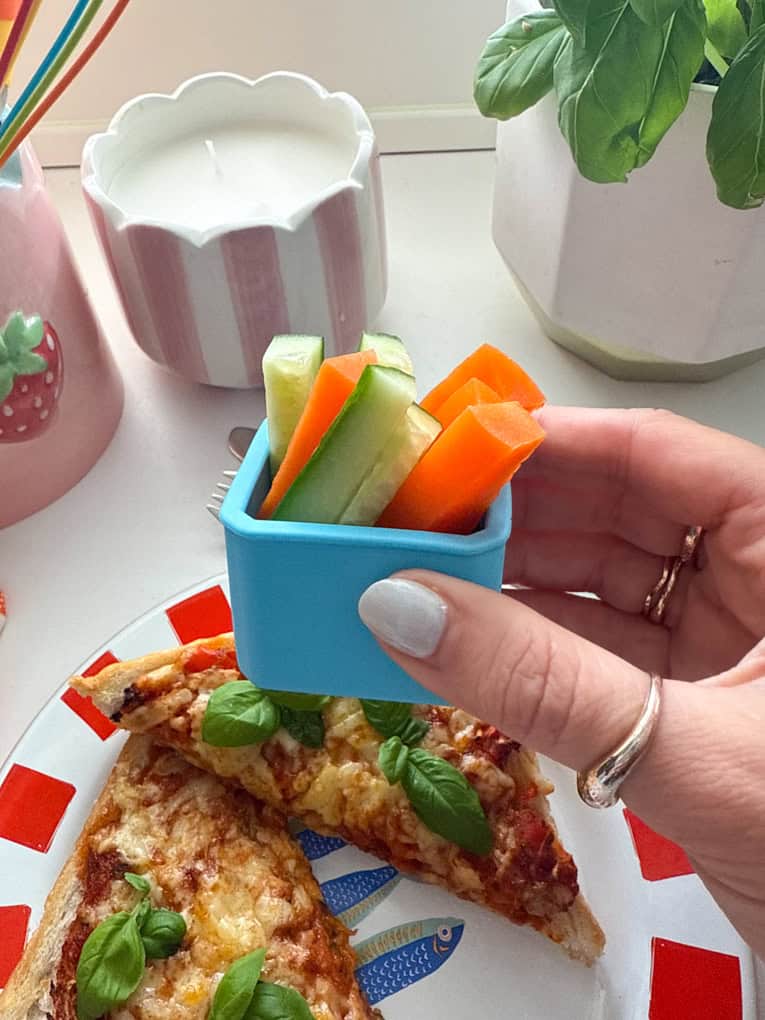Air Fryer Pizza Toast served in  a red & white stripy plate garnished with a sprig of basil and a small blue pot of chopped veggies.