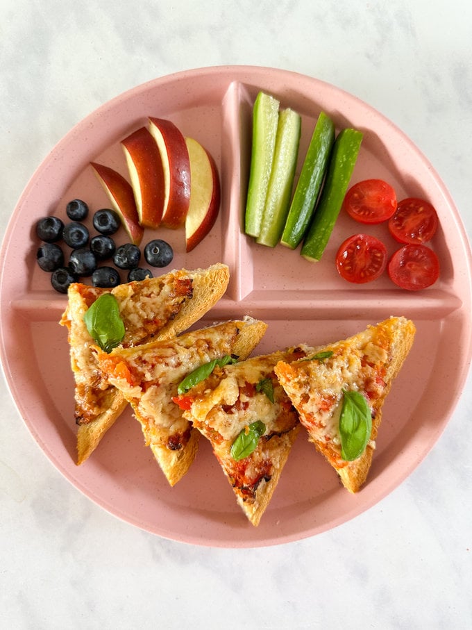 Airfryer pizza toast served on a kids plastic separation plate along with fresh fruit and veggies.