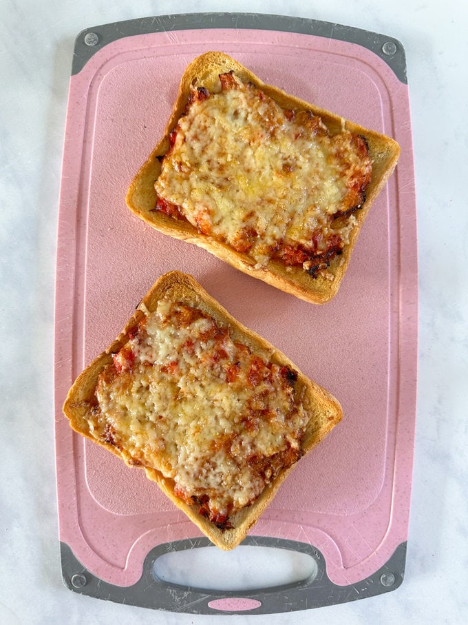 Cooked air fryer pizza toast on a pink chopping board.