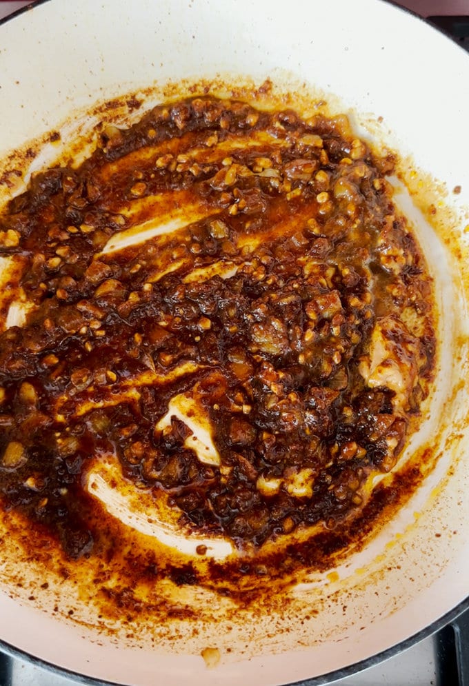 Oil,garlic and curry paste all being added and mixed in a frying pan.