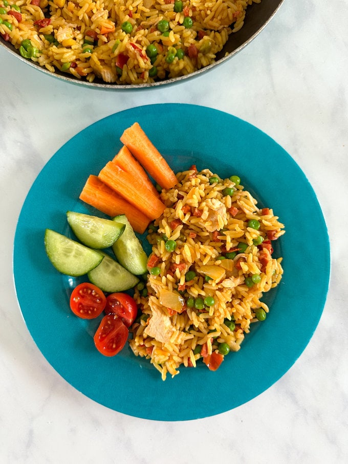 Paella served on a blue child's plate, alongside fresh/chopped carrot's,cucumber and cherry tomatoes.