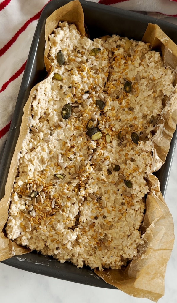 the porridge bread mix in the lined loaf tin topped with mixed seeds