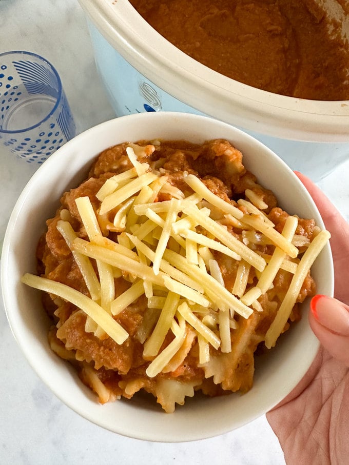 Slow cooker sauce served over pasta and presented in a small round white bowl and garnished with grated cheese.