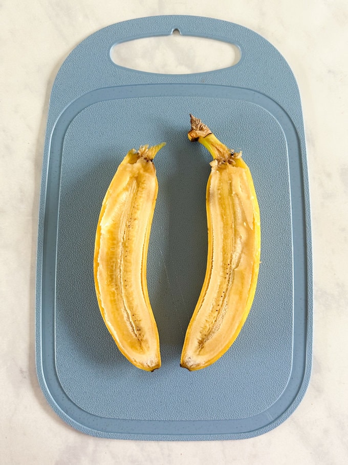 Raw banana cut in half length ways on  a blue chopping board.