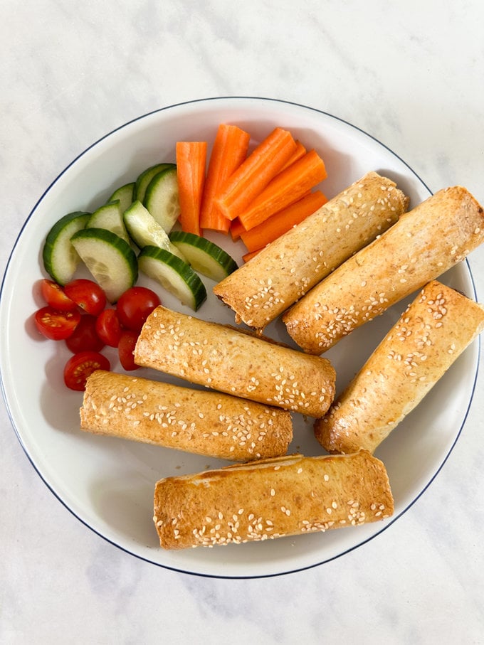 Airfryer Cheats sausage rolls served in an enamel bowl with chopped carrot, cherry tomatoes and chopped cucumber