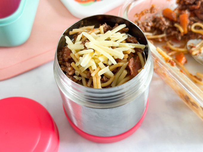 Spaghetti bolognese served in a childs food flask, and garnished with grated cheddar cheese.