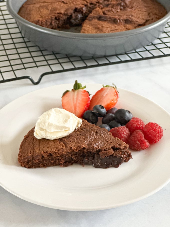 3 ingredient chocolate cake served on a round white plate and garnished with a dollop of Greek yogurt and fresh berries.