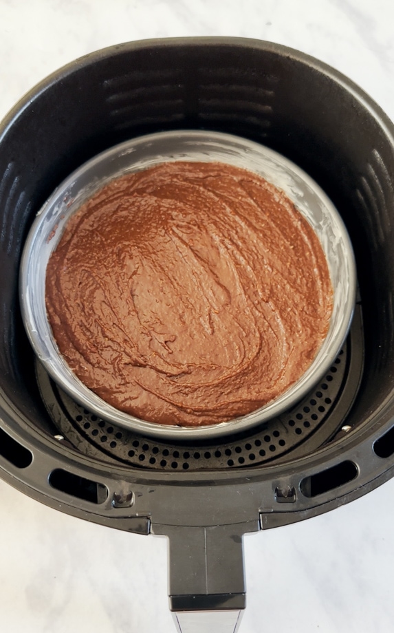Chocolate cake mixture being added to a greased cake tin and then placed in the airfryer.