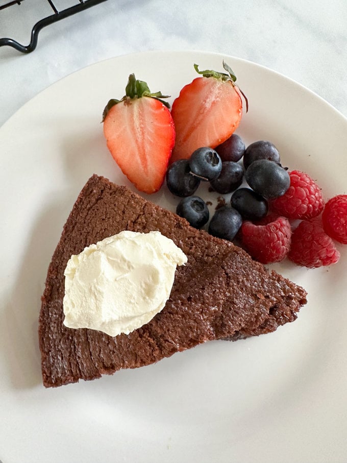 A slice of chocolate air fryer cake served on a white plate. Topped with a dollop of cream and fresh berries