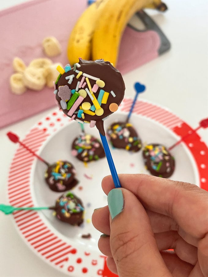 Close up on frozen banana pop, served on a brightly colored blue pick stick. 