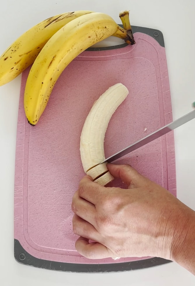 Bananas being chopped into slices on  a pink chopping board.