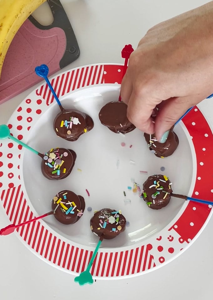 Banana slices laid out in a circle on a plate and coloured sprinkles are being added.