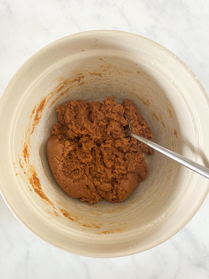 Ingredients being mixed together in bowl with a silver spoon.