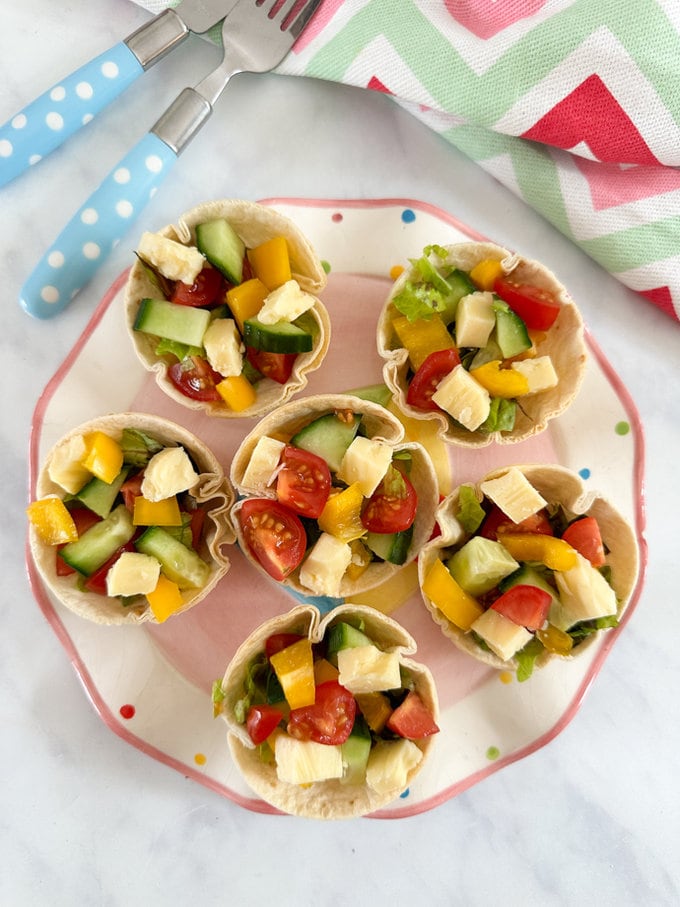 Six Colorful salad cups served on a pink spotty plate. 