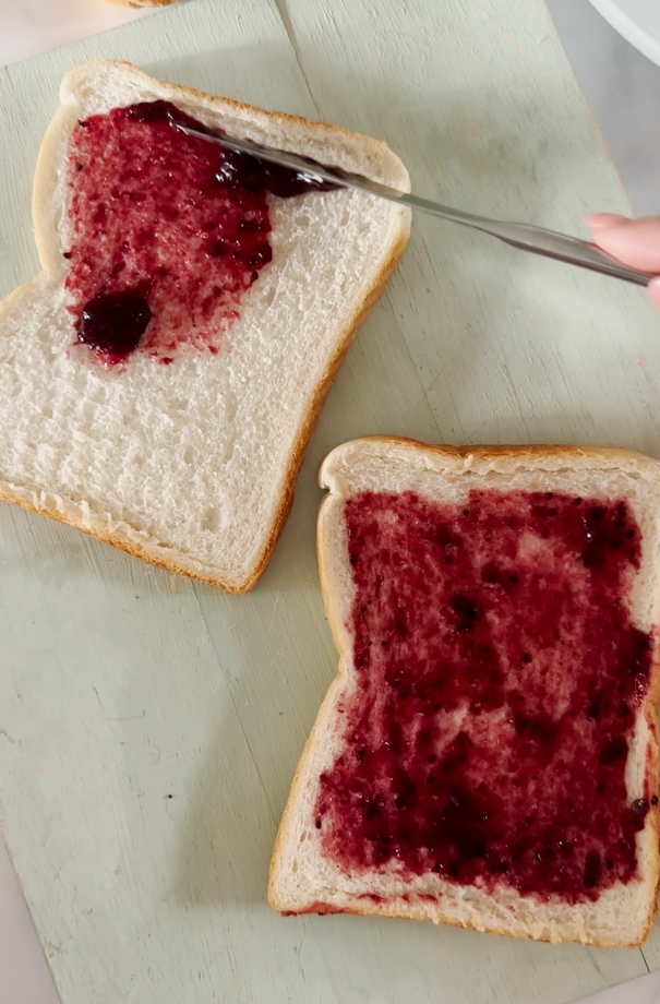Jam being spread onto a piece of white bread with a knife.