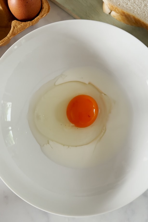 Raw egg cracked into a small white mixing bowl.