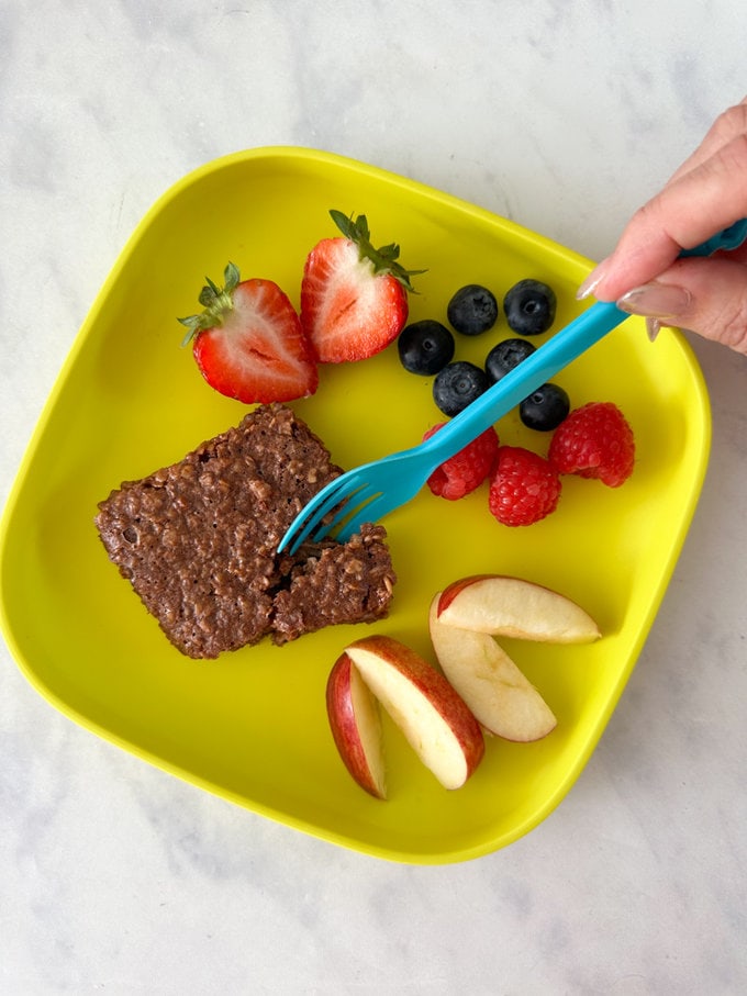 Baked Nutella oat bars served on a bright yellow child's plate and garnished with fresh berries and sliced apple.
