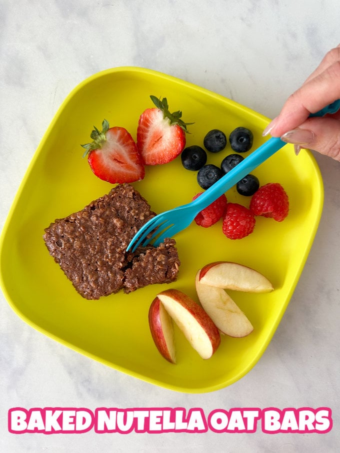 A Baked Nutella oat bar with fresh chopped fruit on a bright yellow square plate with a blue fork