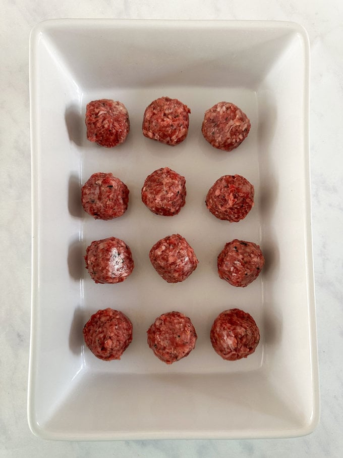 Uncooked meatballs arranged in large white rectangle oven dish, ready for the oven.