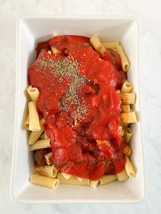 Pasta poured over meatballs and sauce added over the top, ready for the oven.