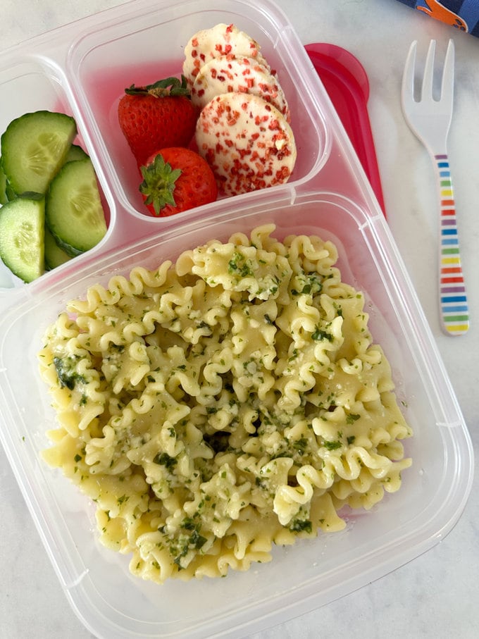 Nut free pesto pasta served in a three compartment clear lunchbox along side fresh chopped cucumber,strawberries and sweet rice cakes.