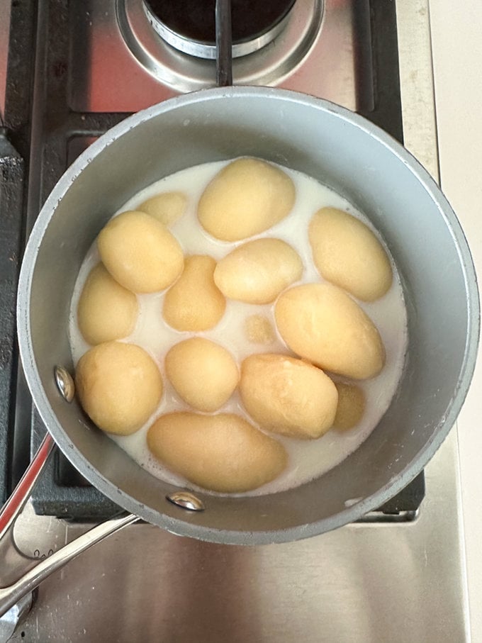Tinned potatoes in a saucepan with some milk added.
