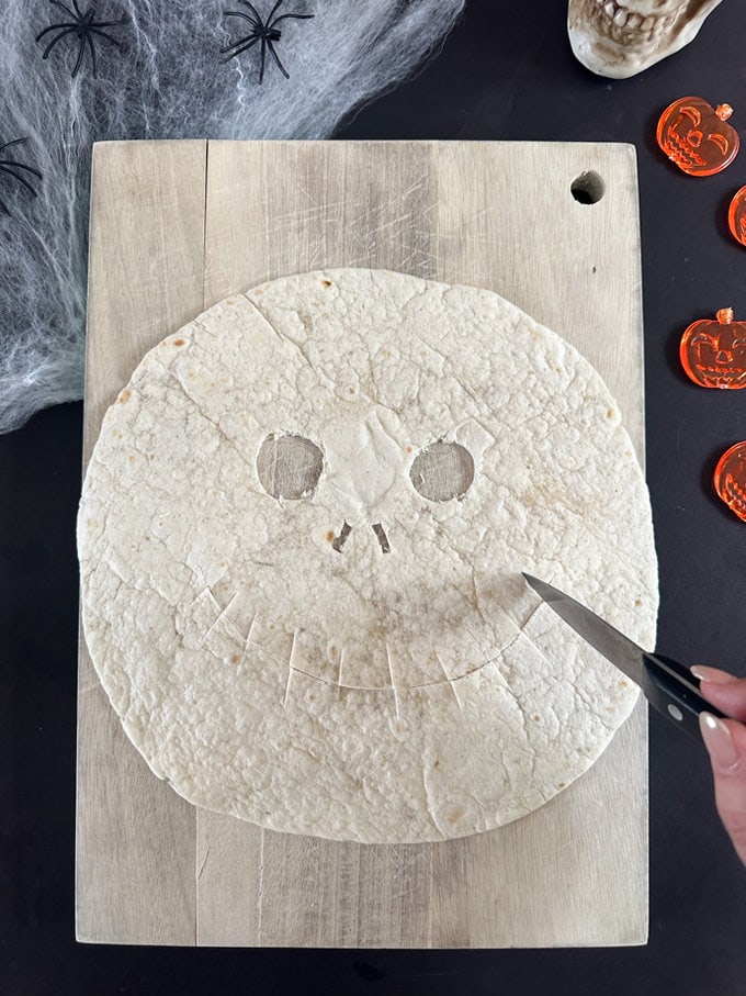 Face being cut out of the tortilla with a sharp knife.