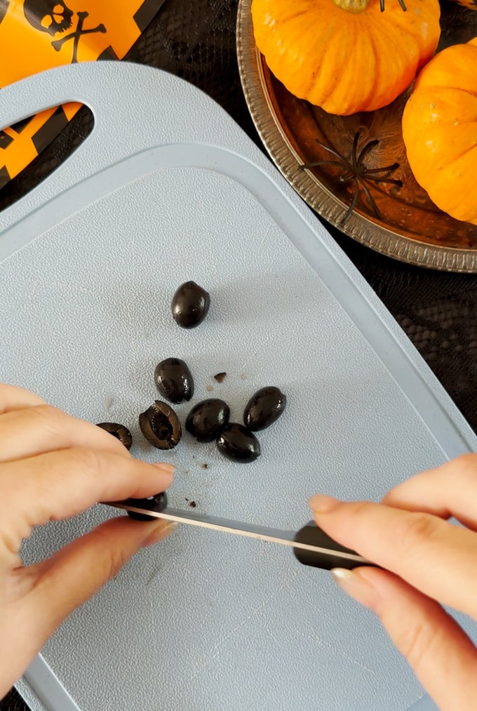 Olives being cut into halves on a chopping board.