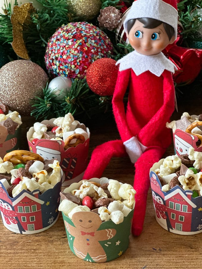 Elf ob the shelf sitting with muffin cases full of trail mix.