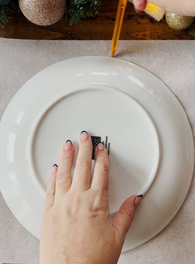 A large white plate is being drawn around to make the wreath template.