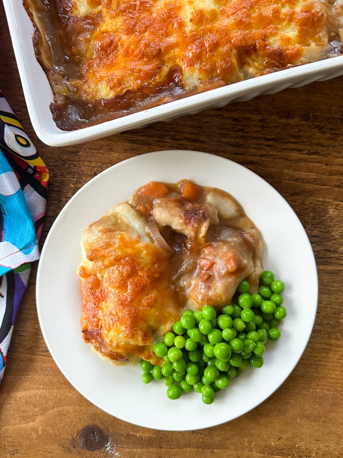 Sausage and mash pie served on a white round dinner plate and garnished with green peas.