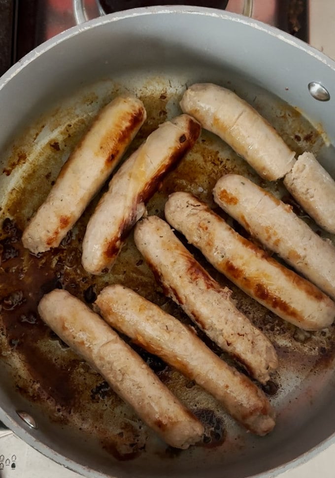 Sausages frying off in a pan, until golden brown.