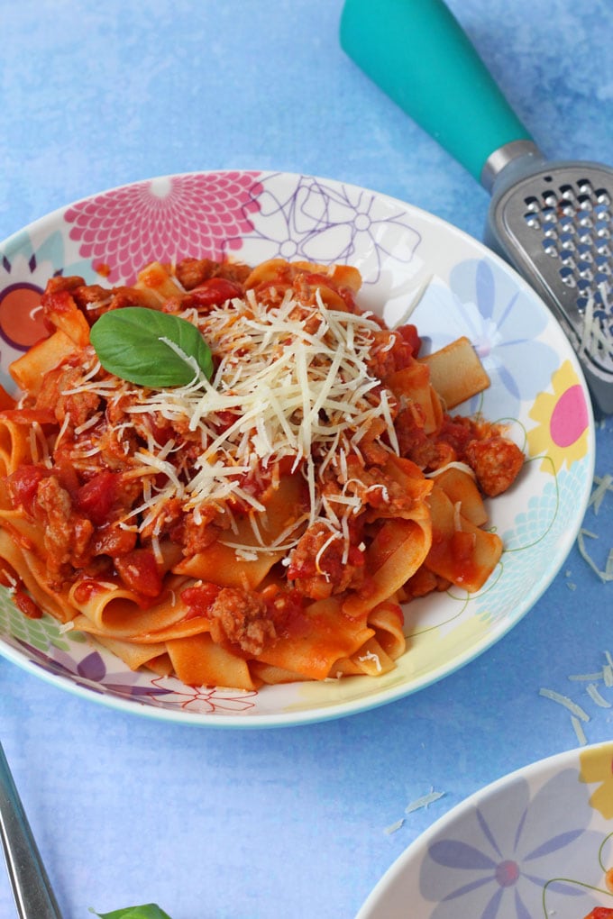 sausage ragu served in a colourful bowl, topped with grated cheese and a fresh basil leaf.
