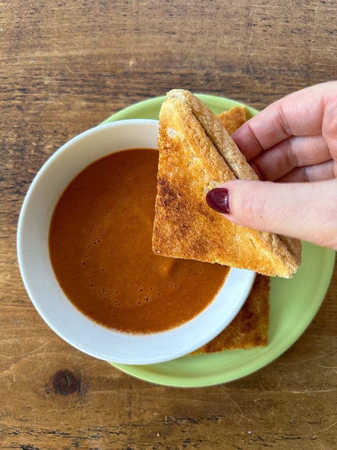 Slice of white bread being dipped into a bowl of hot soup.