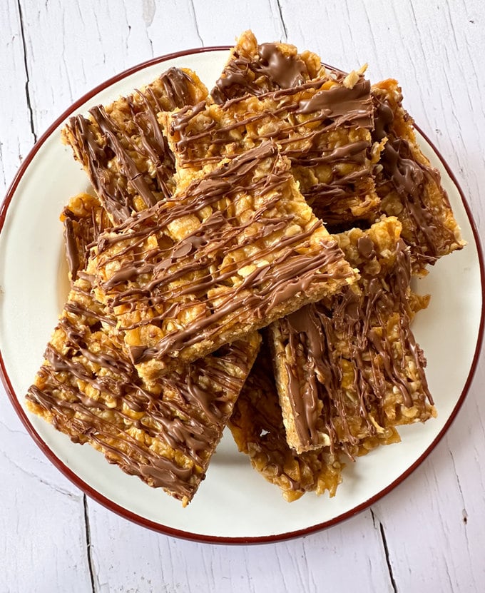 No bake cornflake cakes,cut up into square shaped pieces and arranged on a white dinner plate, and drizzled in milk chocolate. 